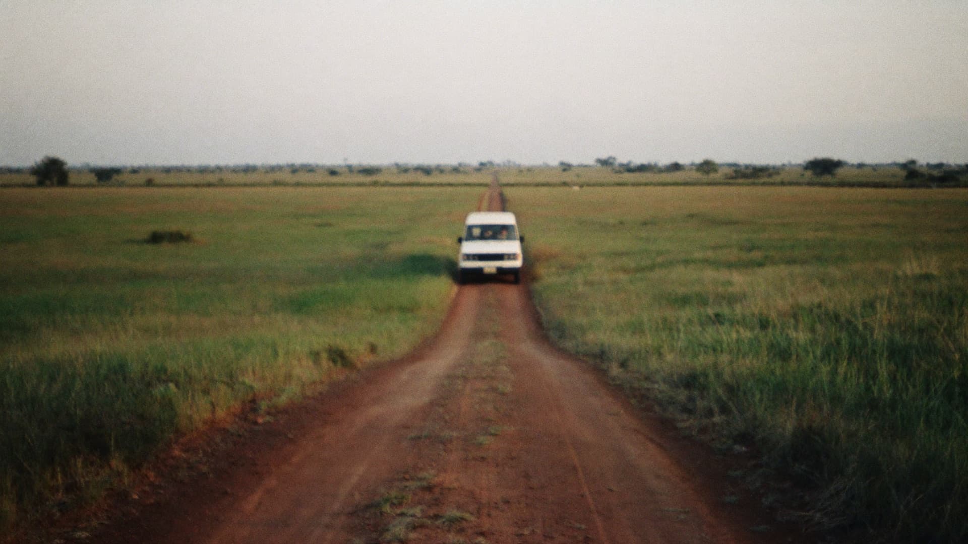 A white vehicle on a red-earth road through green grassland