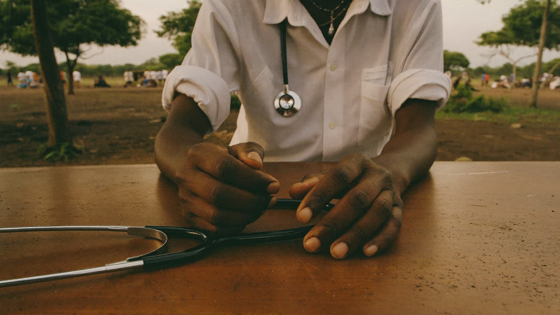 A health worker's hands resting on a wooden table beside a stethoscope